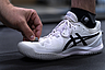 Hand befestigt kleinen runden Sensor an weißem Sportschuh mit schwarzem Muster und schwarzer Socke.